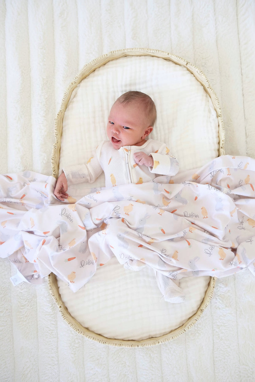 baby boy laying in basket with a white gauze swaddle blanket wearing the sweet peep bamboo waffle zipper footie with a matching personalized swaddle over them 
