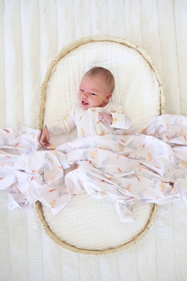 baby boy laying in basket with a white gauze swaddle blanket wearing the sweet peep bamboo waffle zipper footie with a matching personalized swaddle over them 