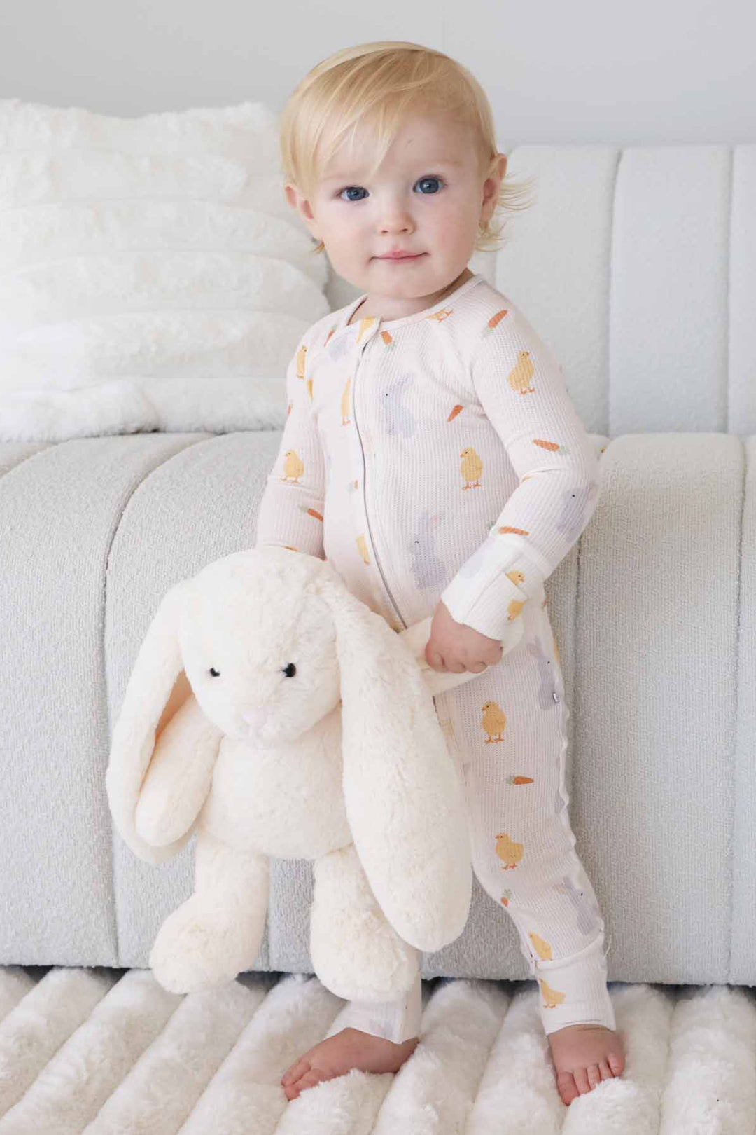 standing baby boy holding a stuffed bunny wearing a chick, peep and carrot bamboo waffle convertible zip romper pajama for easter 