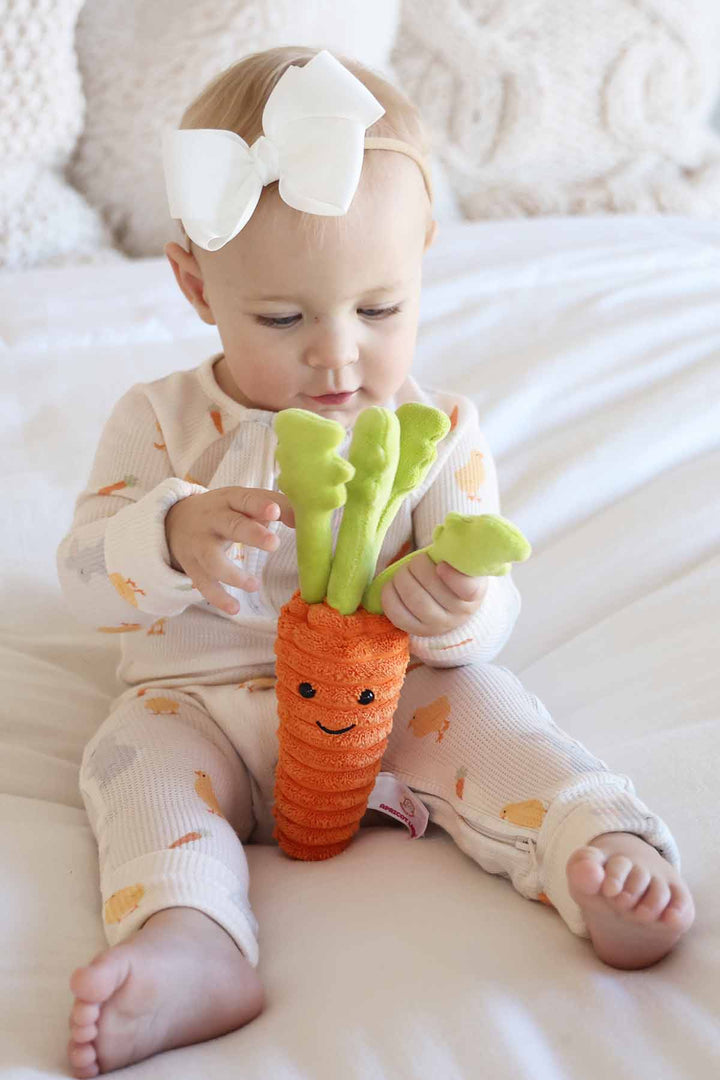 girl wearing neutral easter sweet peep waffle convertible zip romper pj with a white ribbon bow headband and stuffed carrot 