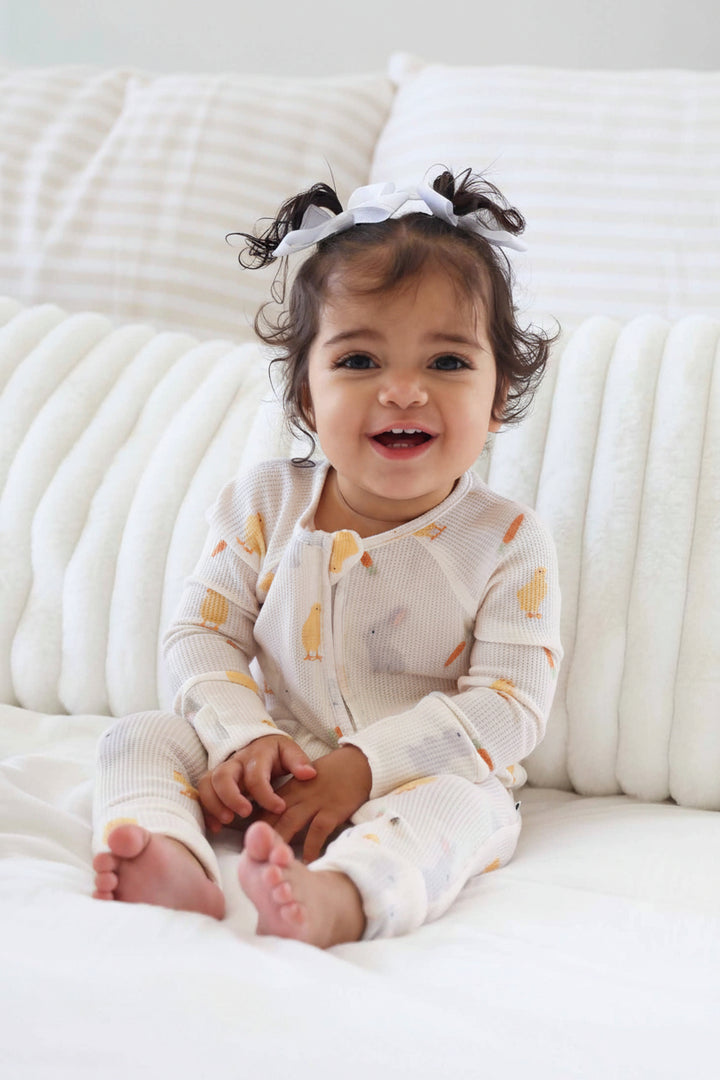 baby girl sitting on couch wearing gender neutral easter bamboo waffle zip romper with chicks, bunnies and carrots 