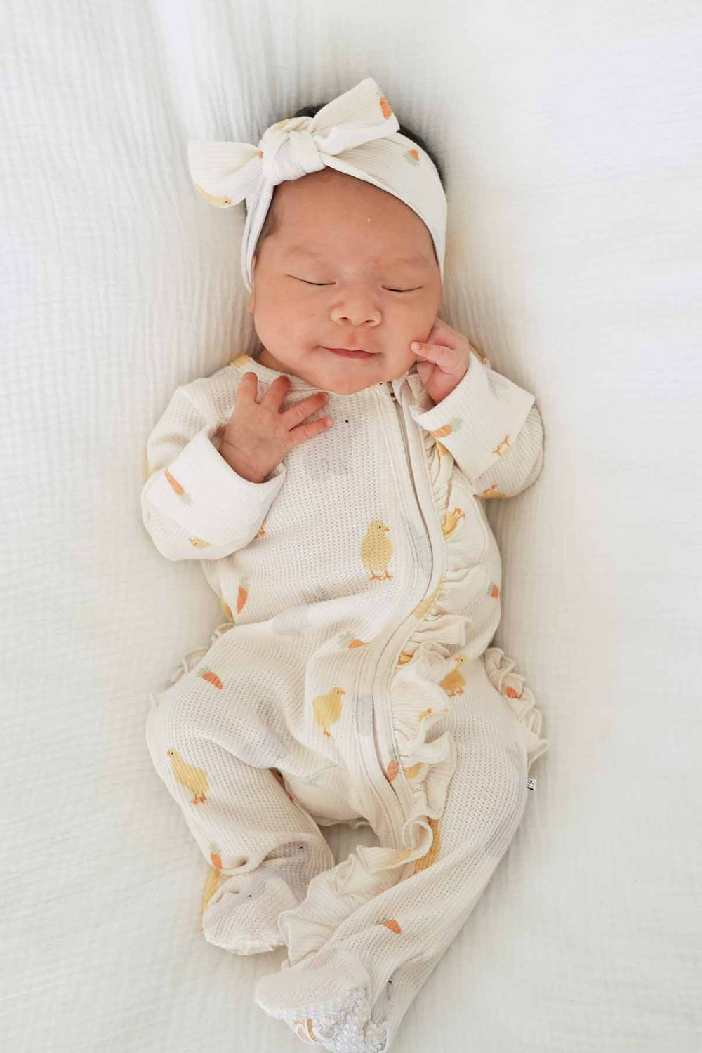 baby girl laying on white blanket in neutral easter bamboo waffle ruffle footie with a matching headwrap 