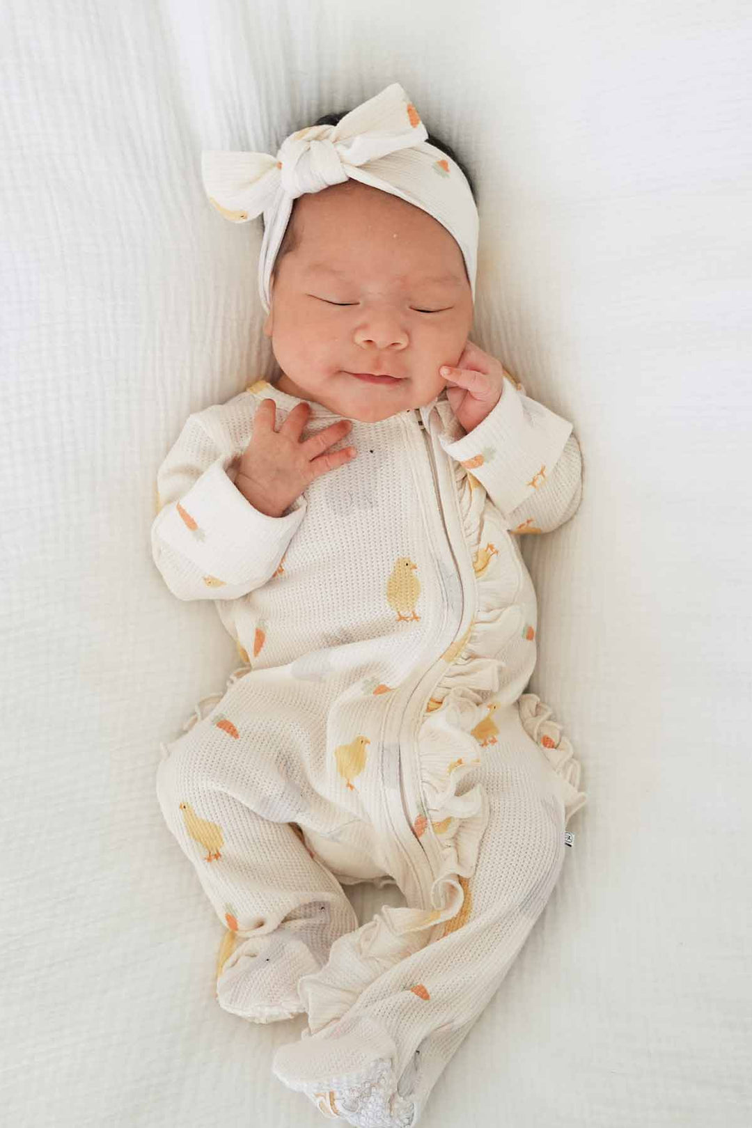 baby girl laying on white blanket in neutral easter bamboo waffle ruffle footie with a matching headwrap 