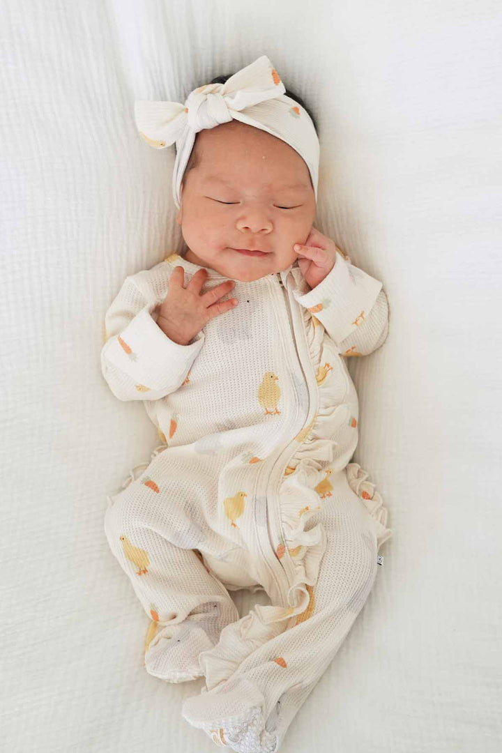 baby girl laying on white blanket in neutral easter bamboo waffle ruffle footie with a matching headwrap 