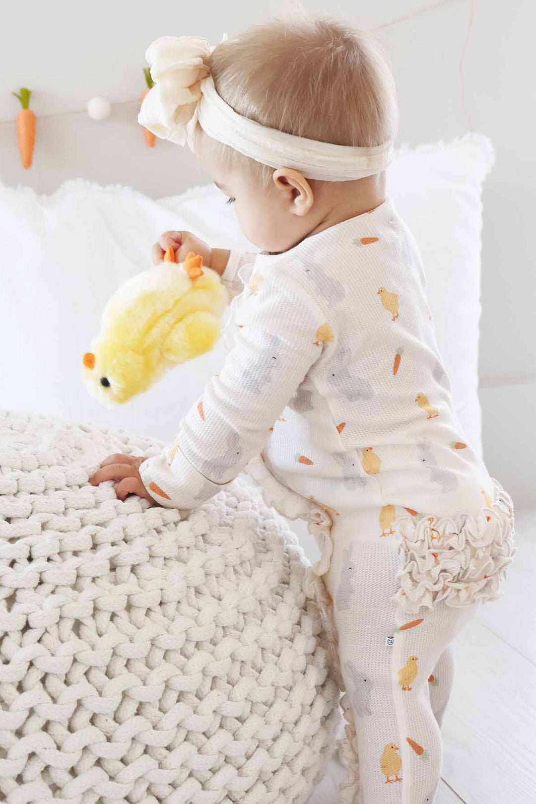 baby girl playing with chick stuffed animal wearing a neutral easter ruffle zipper footie pajama 