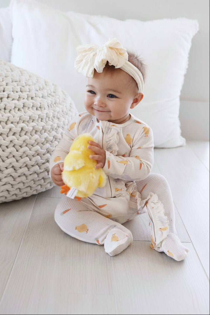 smiling baby girl wearing a sweet peep bamboo waffle ruffle zipper footie and holding a stuffed chick