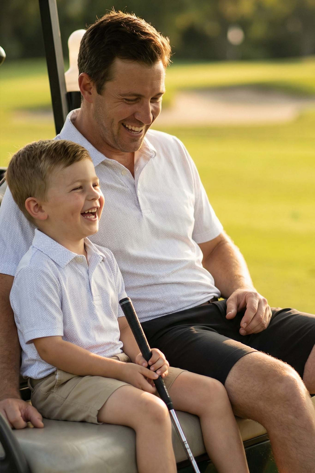 father and son riding on golf cart in matching golf themed polo shirts 