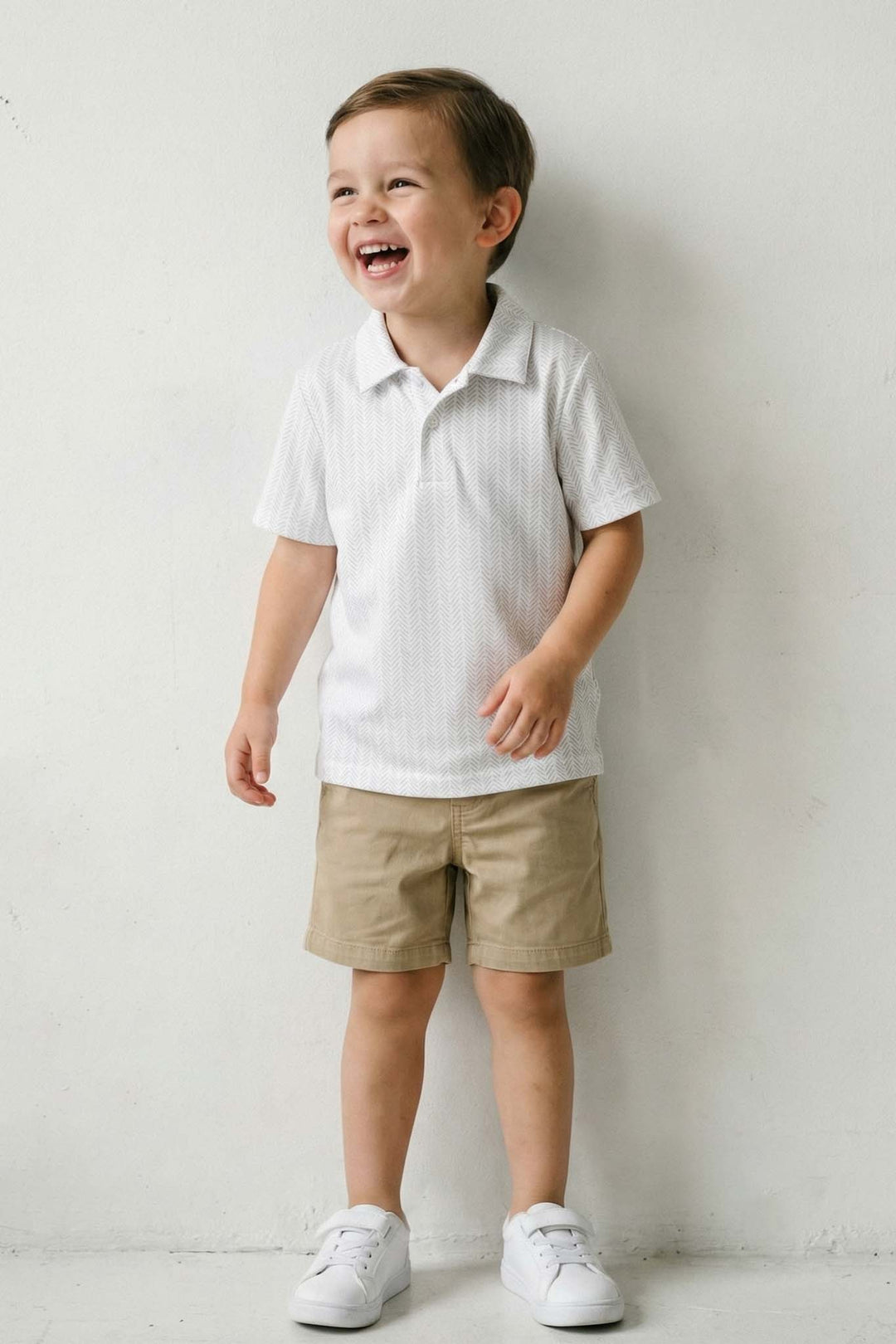 boy standing against wall wearing white polo shirt with golf balls and tees