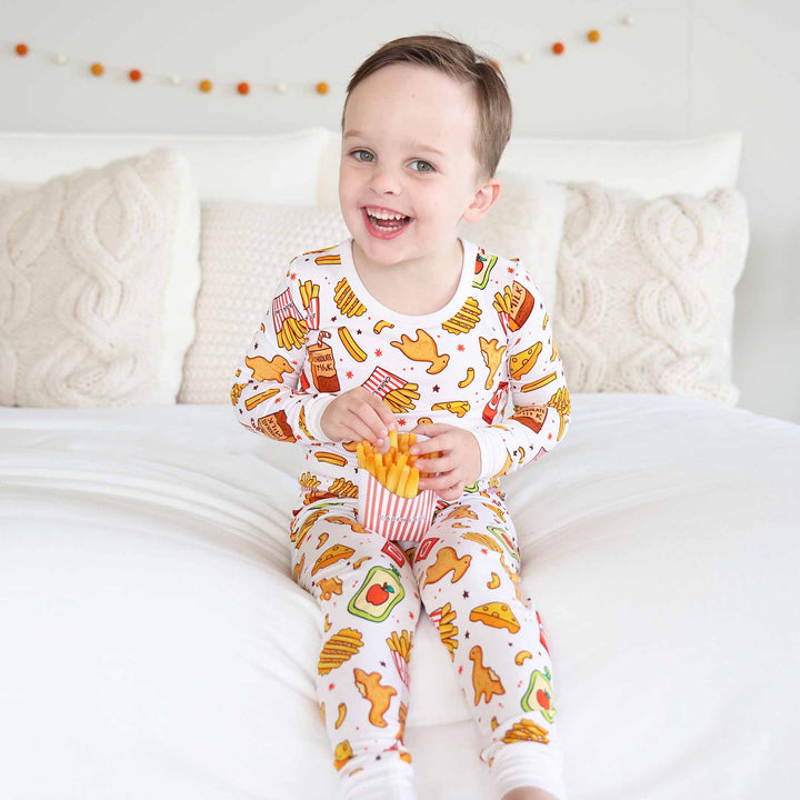 boy sitting on bed in food themed pajama set holding french fries 