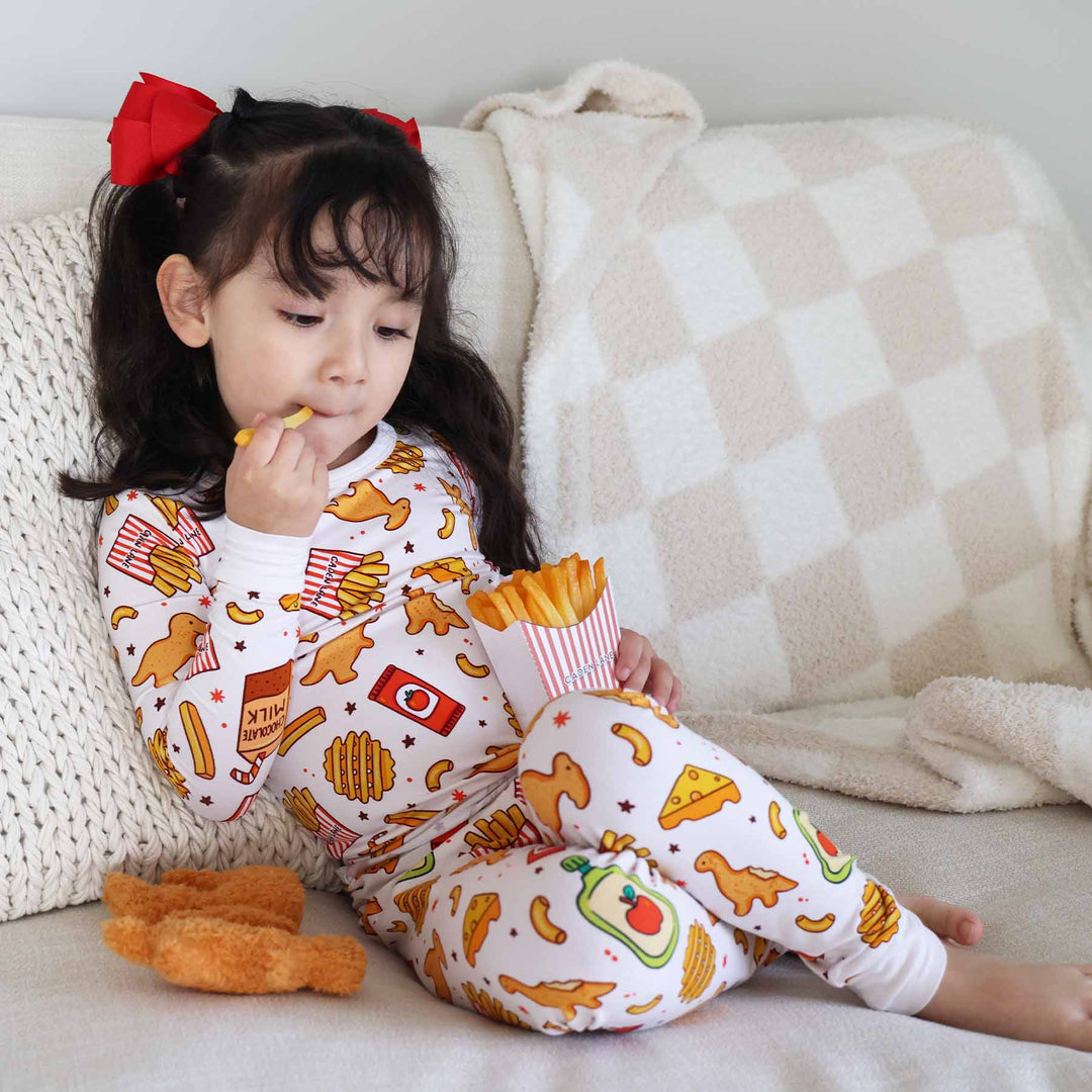 girl leaning back on bed chewing on french fry in fast food themed pajama set 