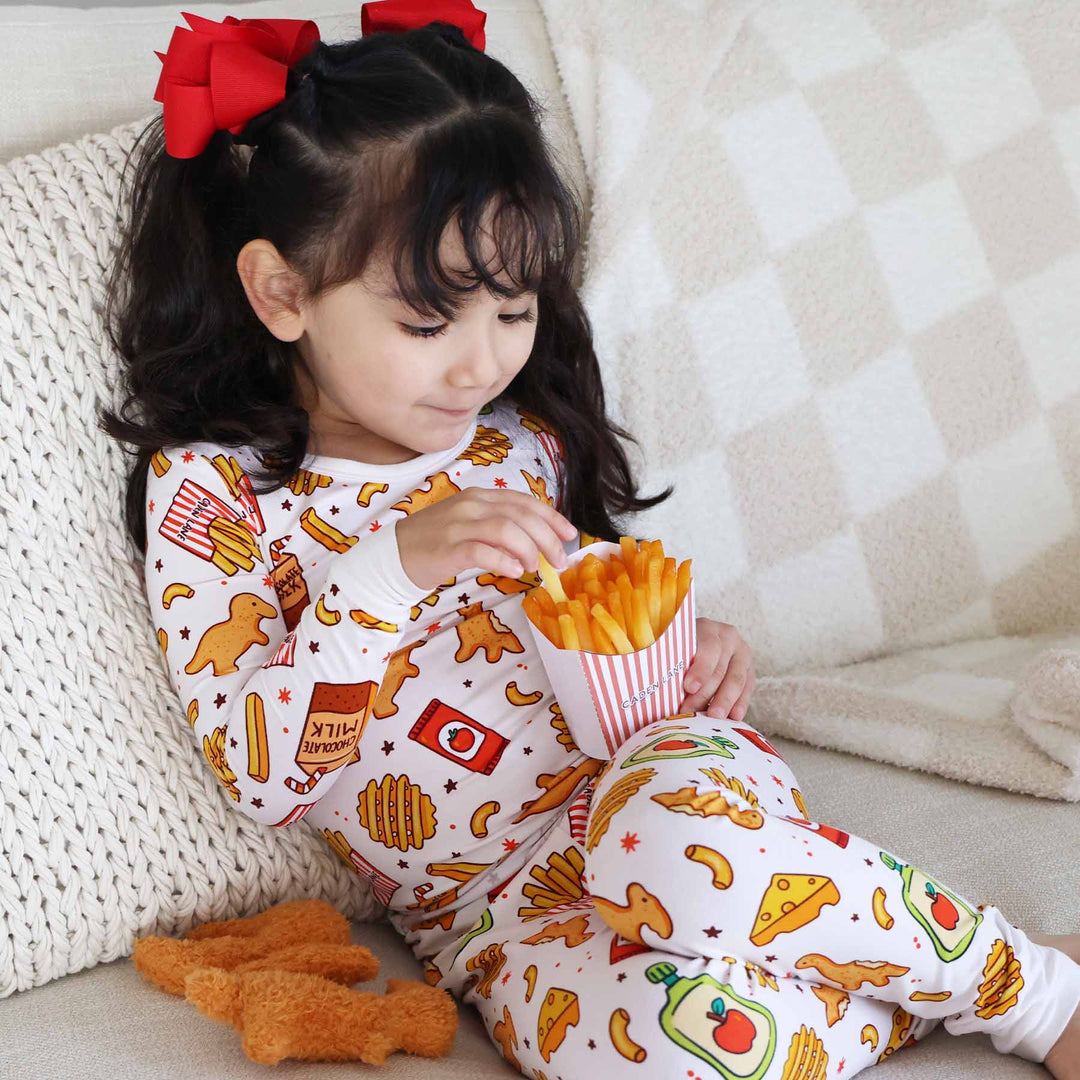 girl wearing tiny bites two piece pajama set holding french fries  with dino chicken nuggets next to her