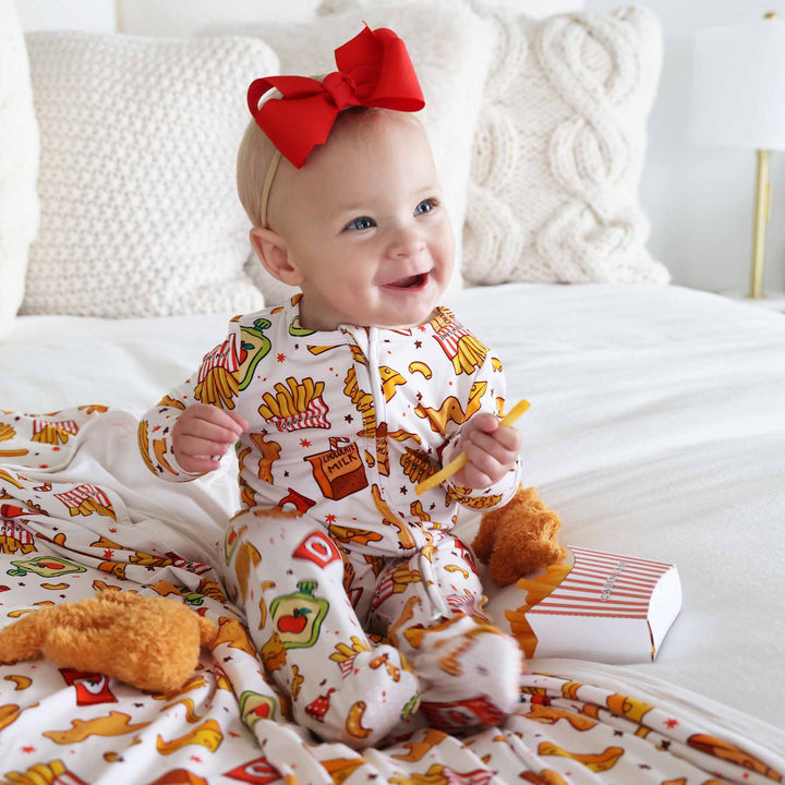 girl wearing a fast food themed baby footie holding a french fry with a red ribbon bow headband 
