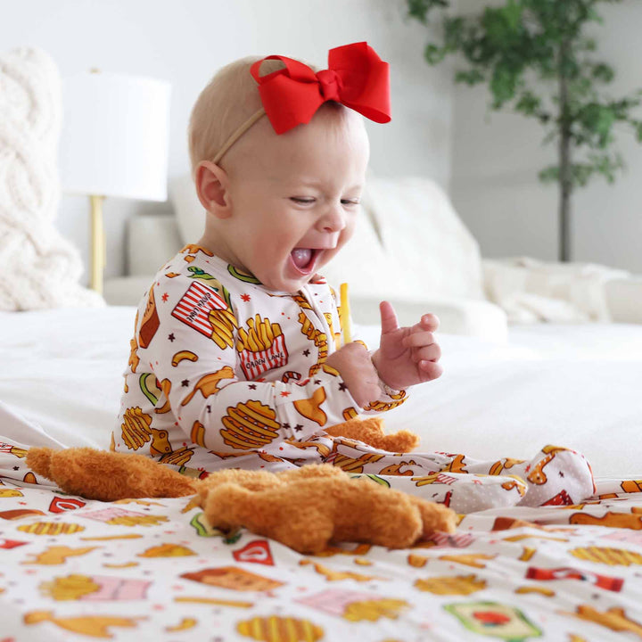 baby girl wearing a fast food themed baby footie holding a french fry with a red ribbon bow on her head 