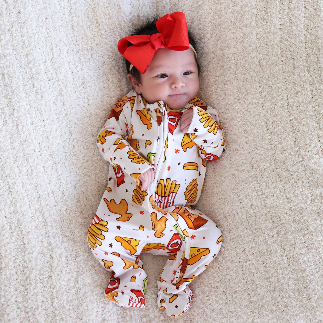 baby girl laying down wearing a fast food themed footie pajama with chicken nuggets, fries and more 