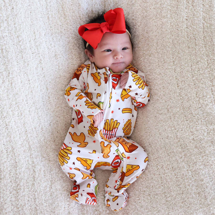 baby girl laying down wearing a fast food themed footie pajama with chicken nuggets, fries and more 