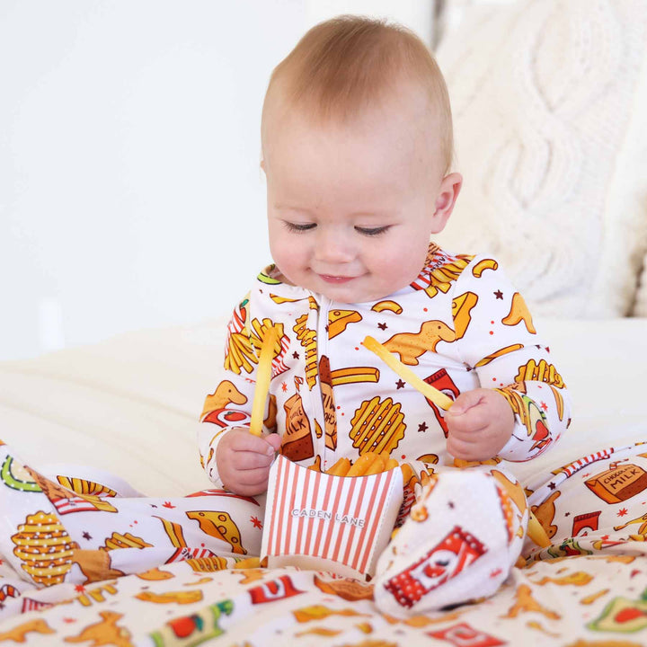 baby wearing a snack themed footie pajama holding french fries with a caden lane logo french fry box
