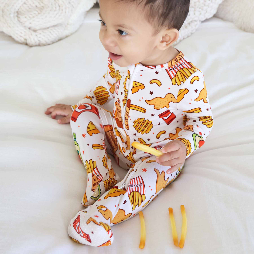 baby sitting on a bed wearing a bamboo viscose baby zipper footie holding a french fry 