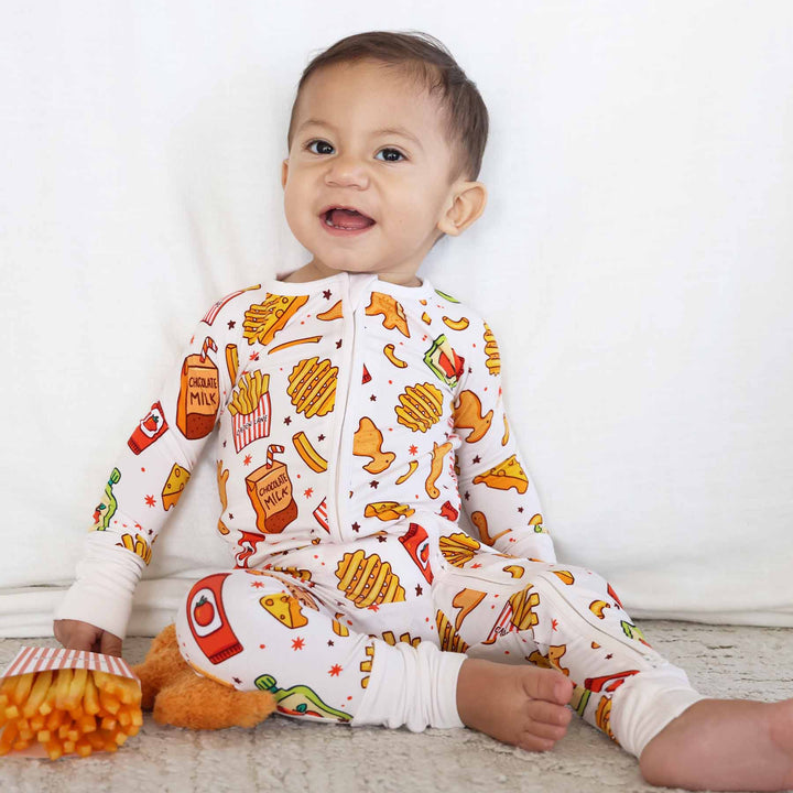 boy sitting down wearing a food themed convertible zip romper sitting next to french fries and dino chicken nuggets 