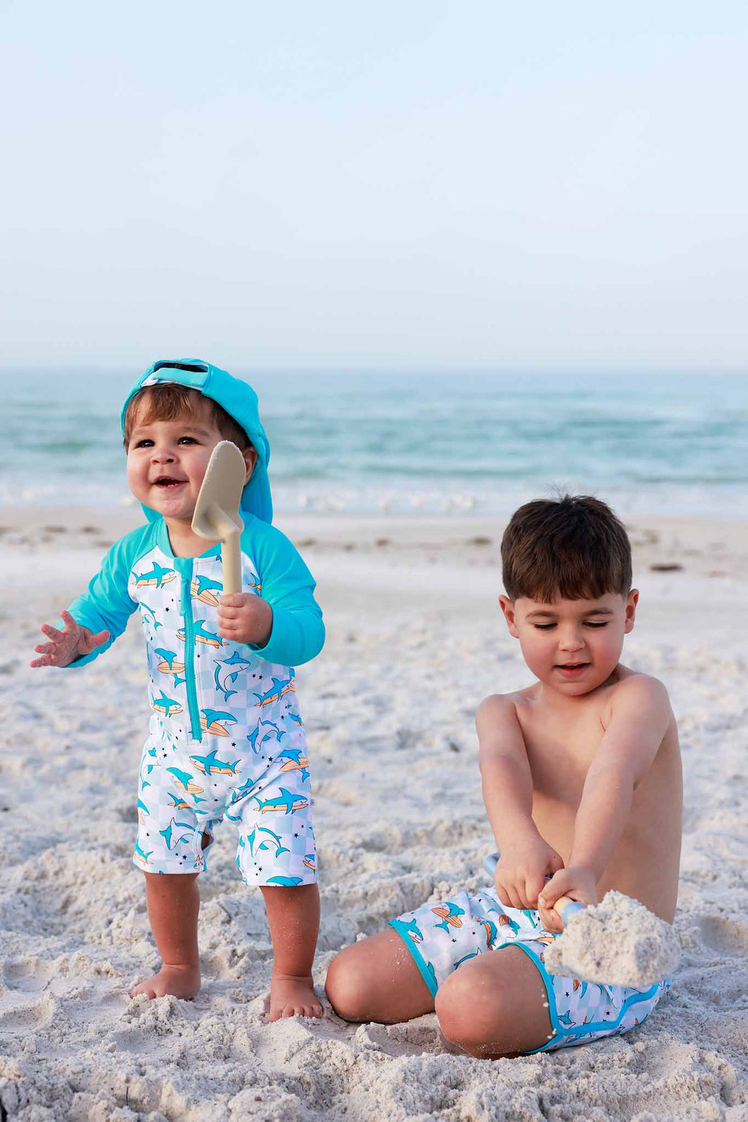 two boys playing on the beach in matching surfing shark swimsuits 