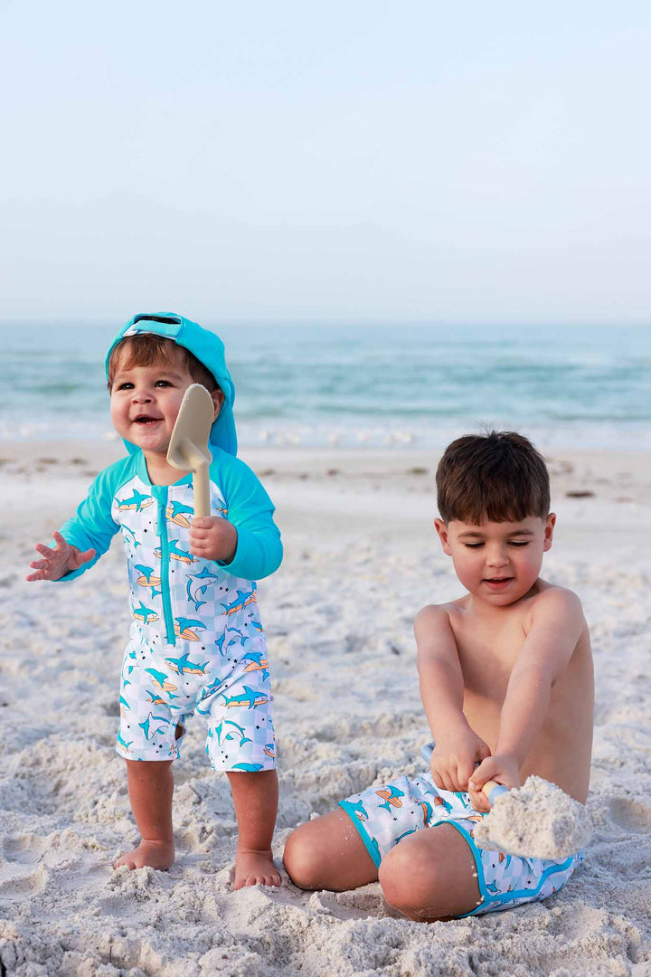 two boys playing on the beach in matching surfing shark swimsuits 