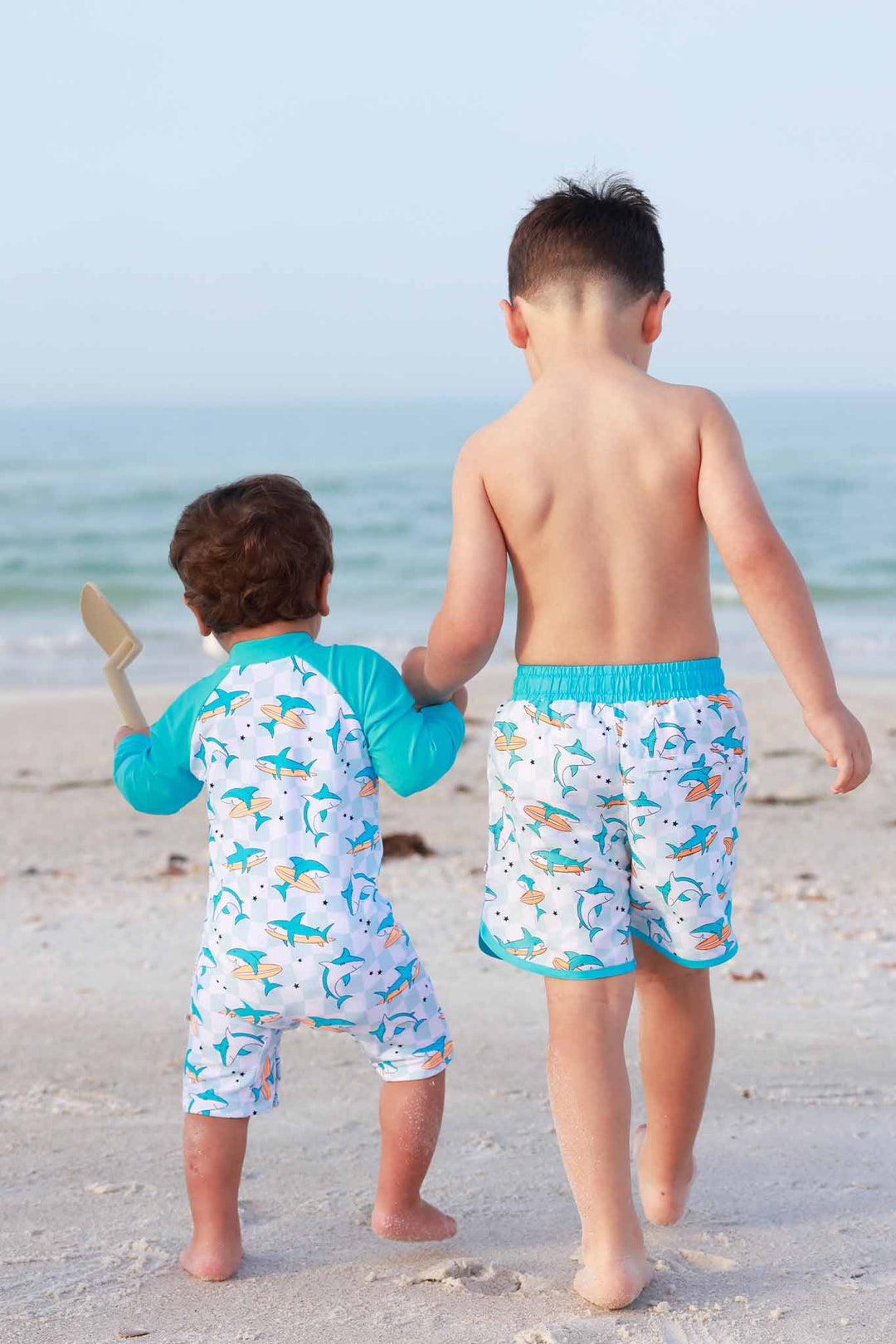 brothers walking on the beach holding hands in totally jawsome matching swimsuits 