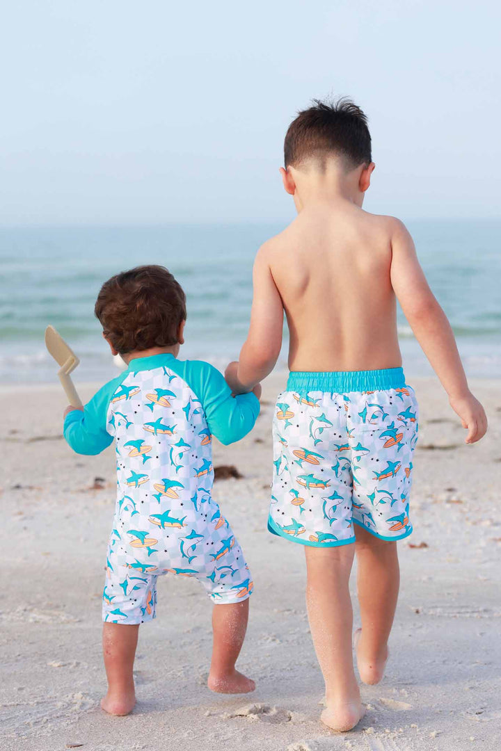 brothers walking on the beach holding hands in totally jawsome matching swimsuits 