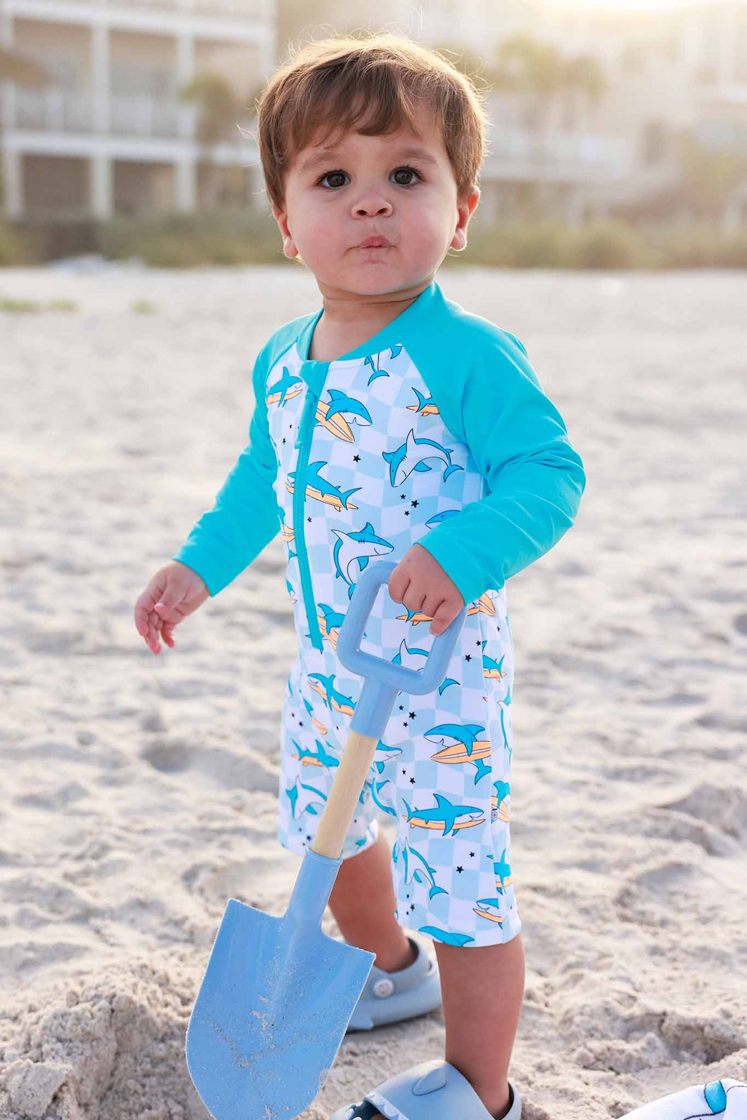 little boy in totally jawsome shortie swim romper holding a beach shovel