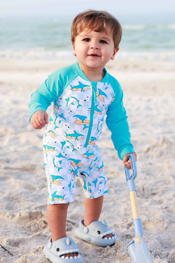 boy digging in sand on beach in shark swim romper shortie 