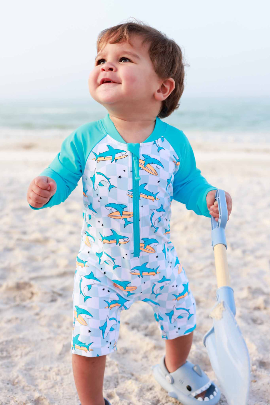 boy walking on beach in totally jawsome long sleeve swim romper shortie with beach shovel 