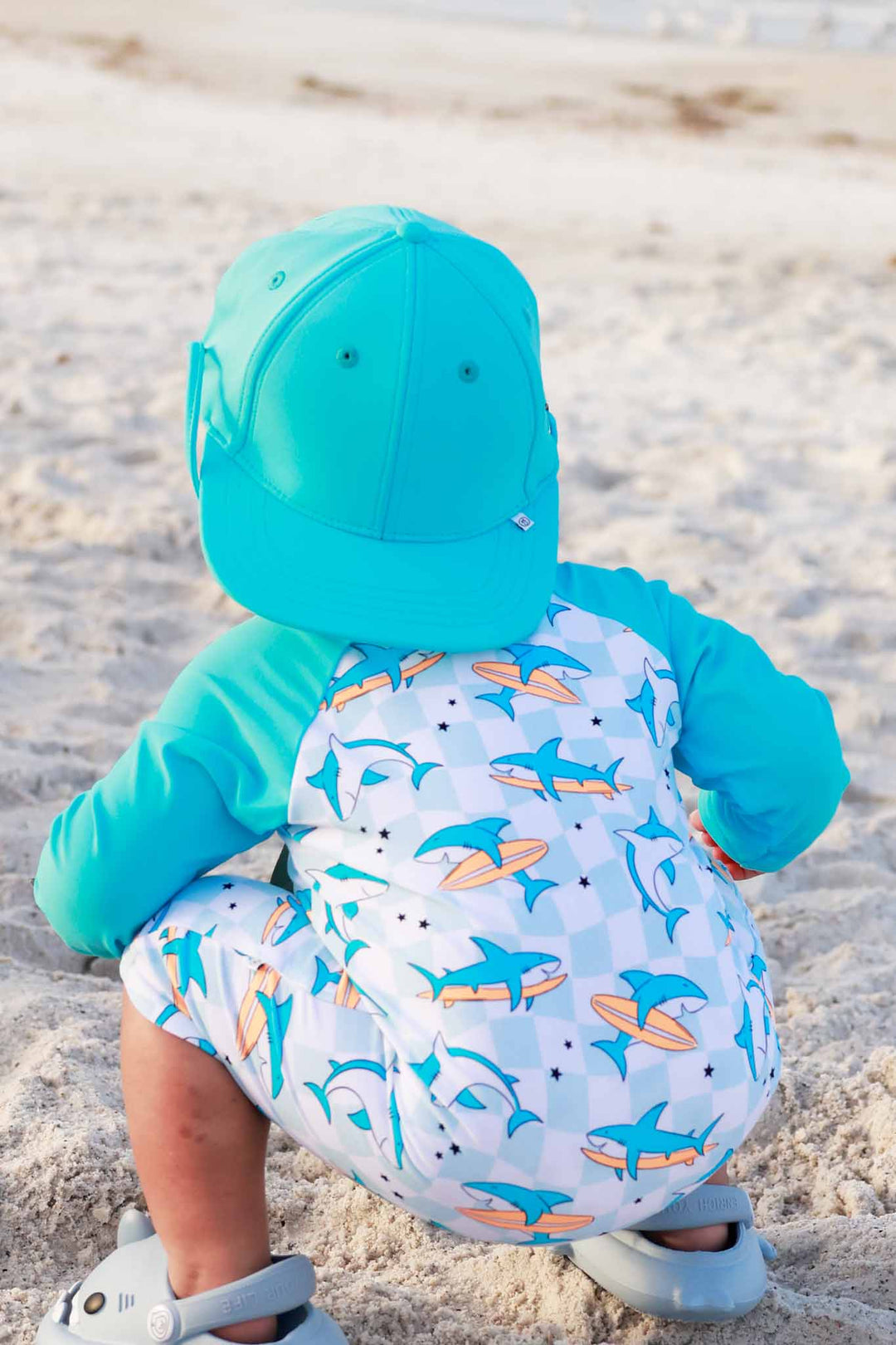 little boy in surfing shark swim romper and turquoise waterproof surf hat 