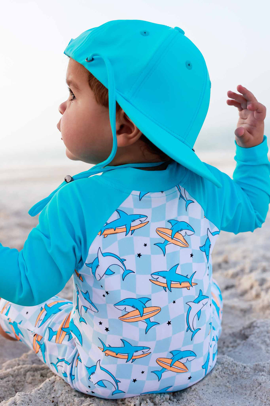 boy sitting on beach in totally jawsome surf hat and matching swim romper