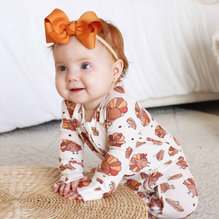 baby wearing a turkey zip romper with orange bow headband 