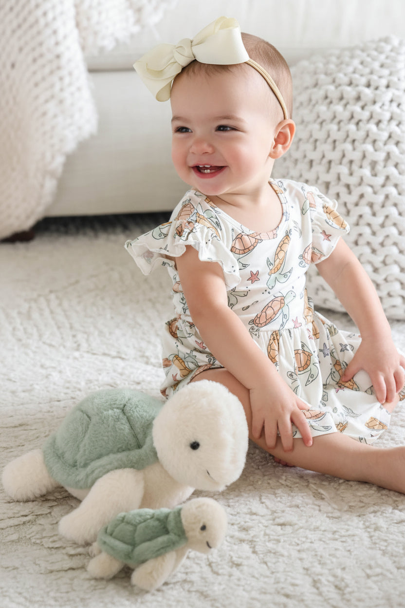 baby girl sitting in turtle bodysuit dress with stuffed turtles next to her