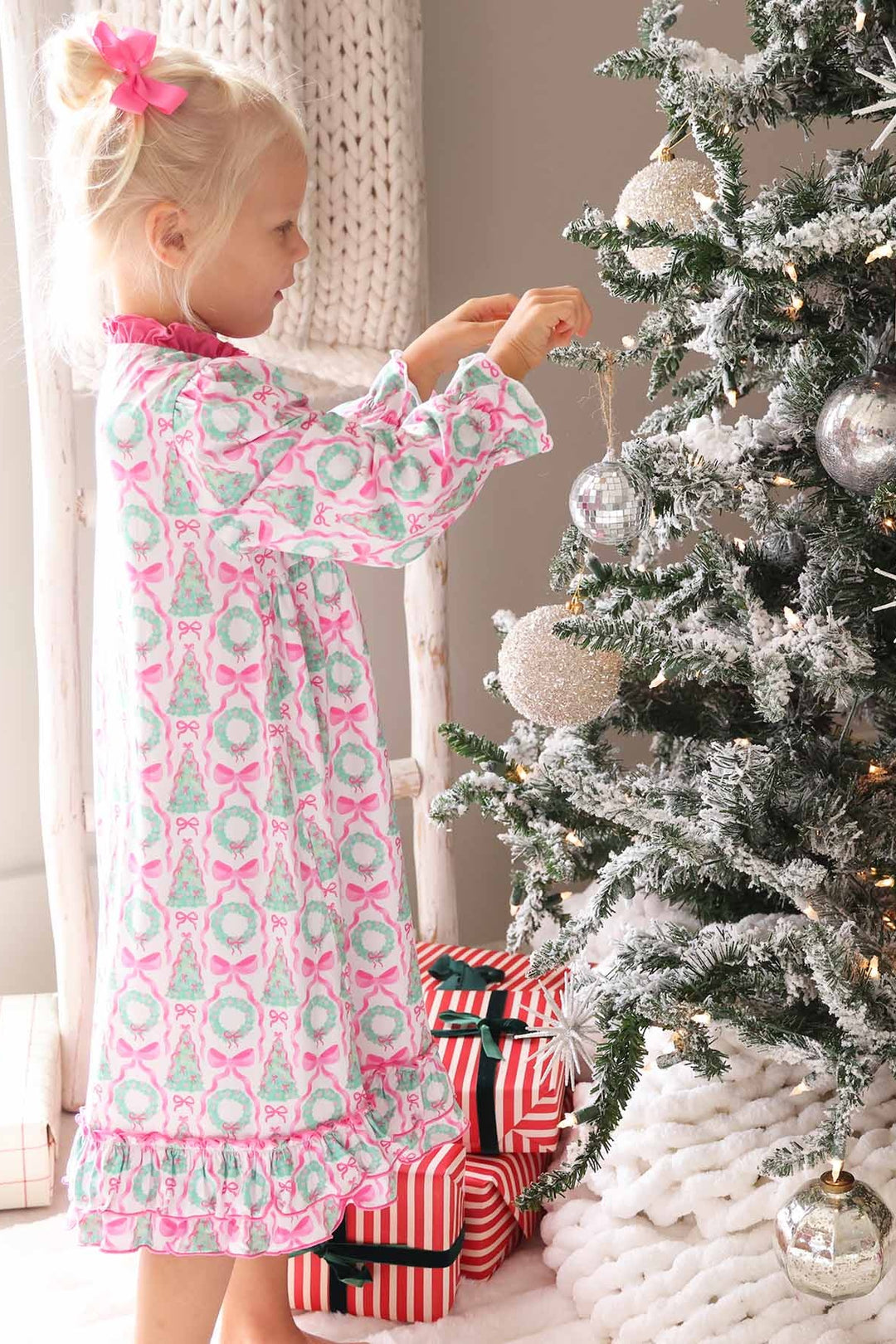 Girl in Caden Lane pink night dress with wreaths and bows standing next to Christmas tree