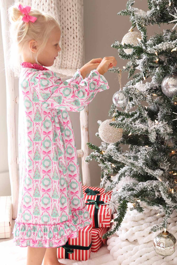 Girl in Caden Lane pink night dress with wreaths and bows standing next to Christmas tree