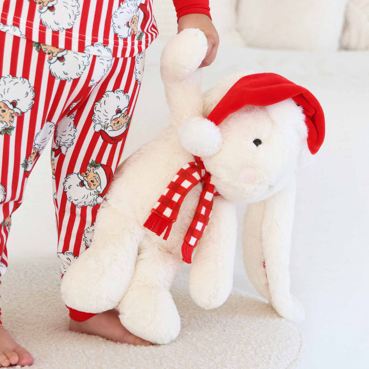kids holding a white bunny stuffed animal wearing a red christmas hat and red and white checkered scarf